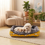 Panier douillet jaune à motifs pour chiens et chiots dans un salon moderne, avec un Bichon Frise et un Cavalier King Charles Spaniel blottis ensemble.
