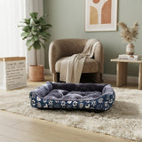 Panier pour chat et petit chien bleu marine à motifs dans un salon moderne et lumineux avec une plante verte et un fauteuil beige.