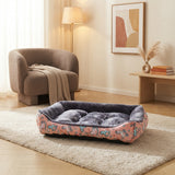 Panier pour petit et moyen chien rose à motifs sur un tapis crème dans un salon moderne avec fauteuil bouclé et plante verte.