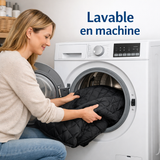 Une femme insère la couverture de siège auto noire et matelassée pour chien dans une machine à laver blanche, illustrant la mention « Lavable en machine »